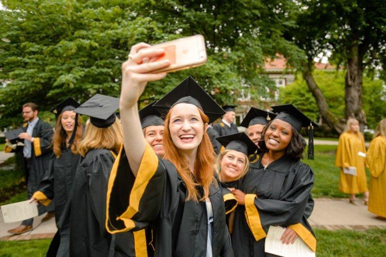 multiple students leaning in for a selfie photo in graduation attire