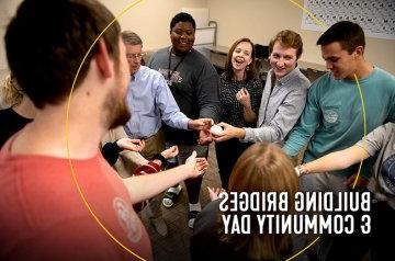 Students, faculty, and staff standing in a circle with hands inside circle touching rock participating in exercise for building bridges